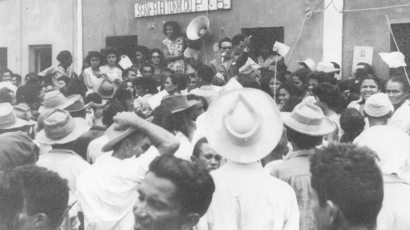 Na foto, de 1954, o líder sindical Floriano Bezerra de Araújo, com impecável paletó de casimira inglesa, comprado no Rio de Janeiro, fala ao povo de Macau em sua primeira candidatura a deputado estadual, na qual conquistou a 1ª Suplência e teve a honra de assumir o mandato por 30 dias. Essa foi a primeira legislatura de mais duas outras que Floriano venceu de forma integral, até o golpe empresarial-militar de 1964, que cassou seu mandato e suspendeu seus direitos políticos por 18 anos